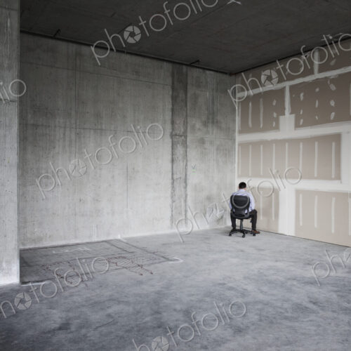 Business person sitting in the corner of a large empty raw office space.