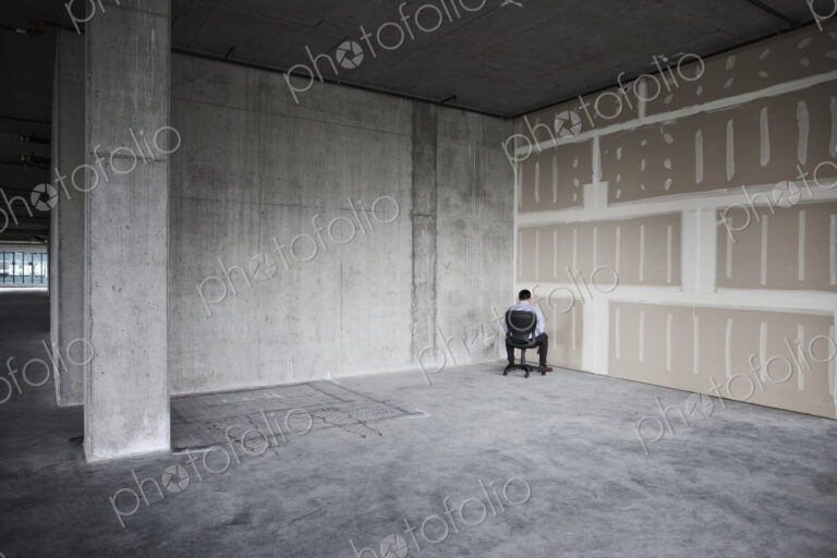Business person sitting in the corner of a large empty raw office space.