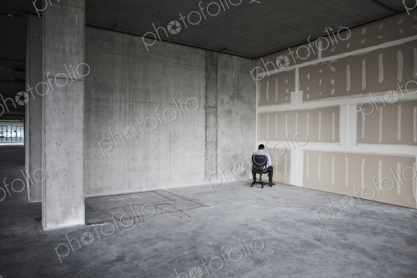 Business person sitting in the corner of a large empty raw office space.