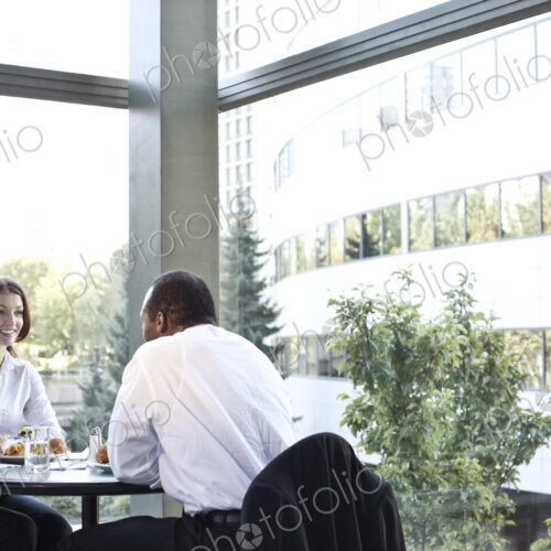Business woman and man in an informal lunch meeting at a table in a open lobby area.