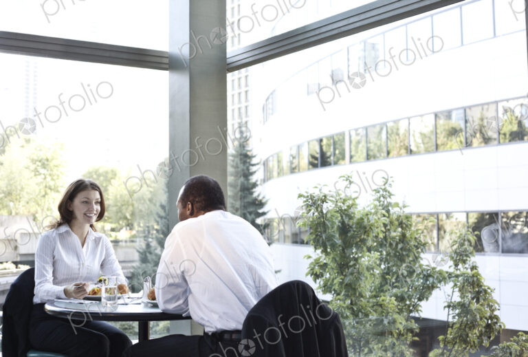Business woman and man in an informal lunch meeting at a table in a open lobby area.