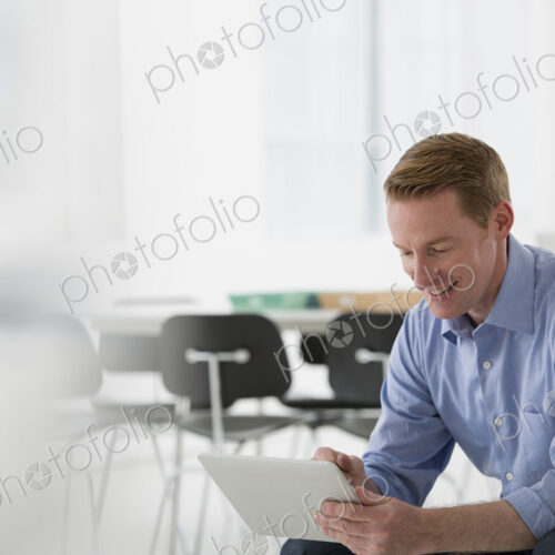 Business. A light airy office environment. A man sitting holding a digital tablet.