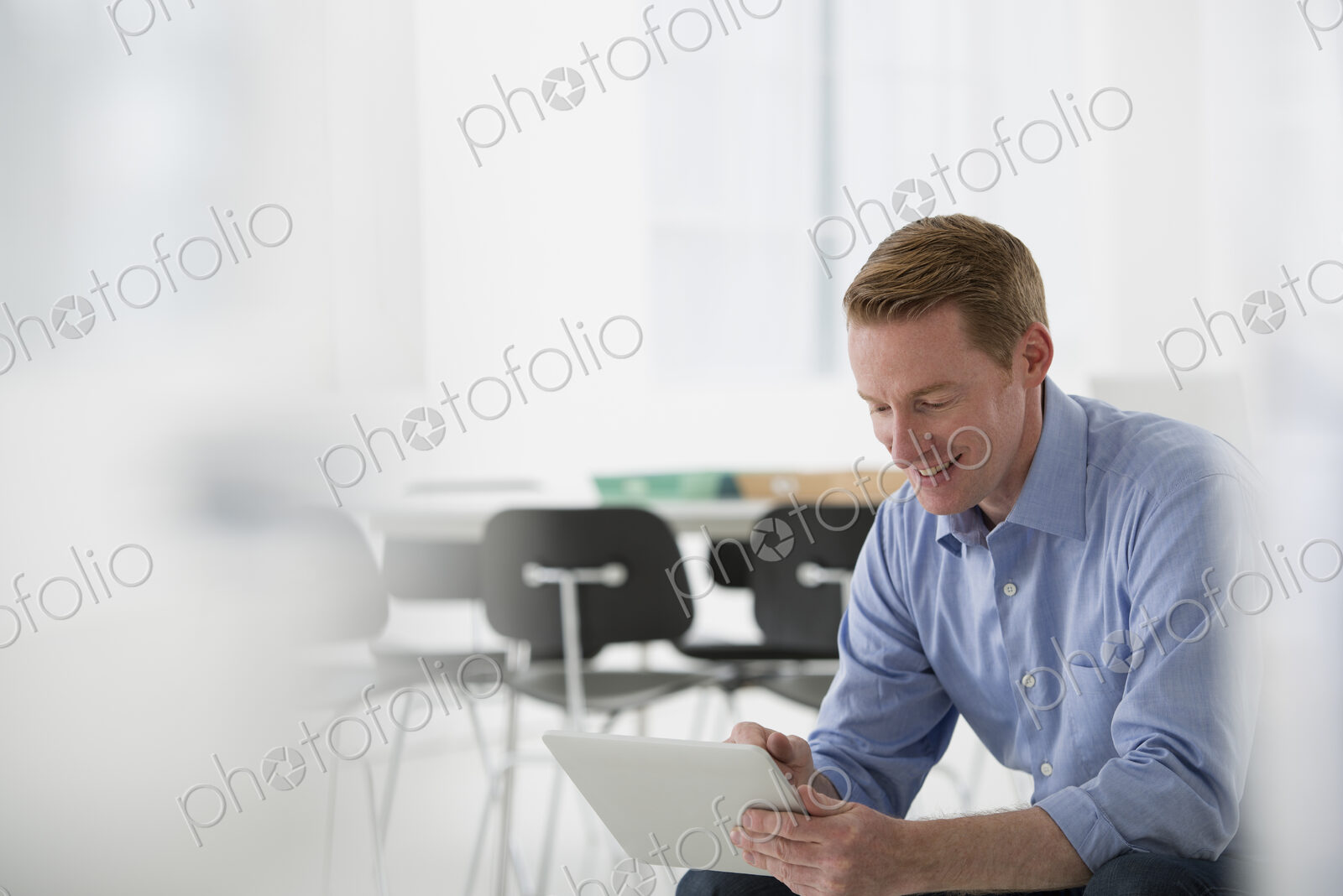 Business. A light airy office environment. A man sitting holding a digital tablet.