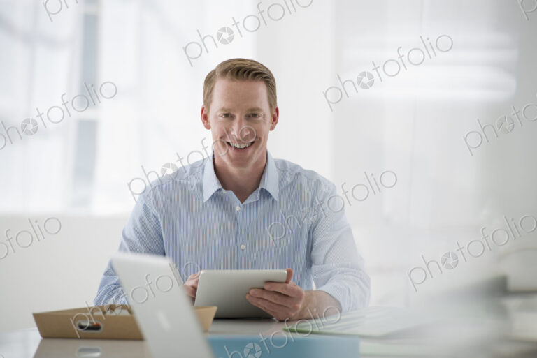 Business. A light airy office environment. A man sitting holding a digital tablet.