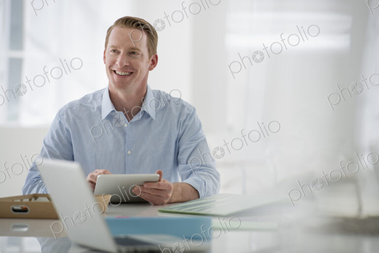Business. A light airy office environment. A man sitting holding a digital tablet.