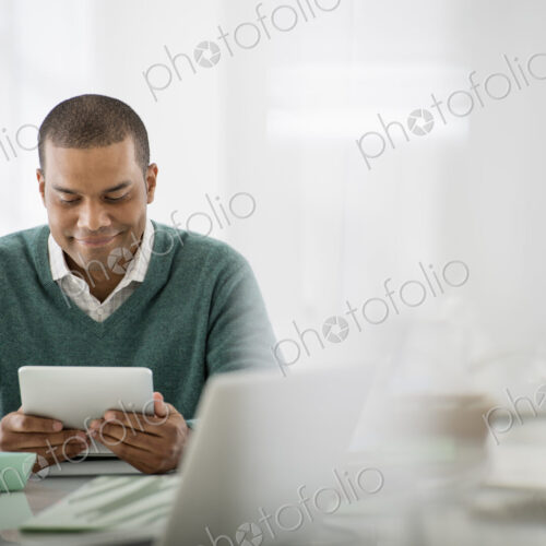 Business. A light airy office environment. A man sitting holding a digital tablet.