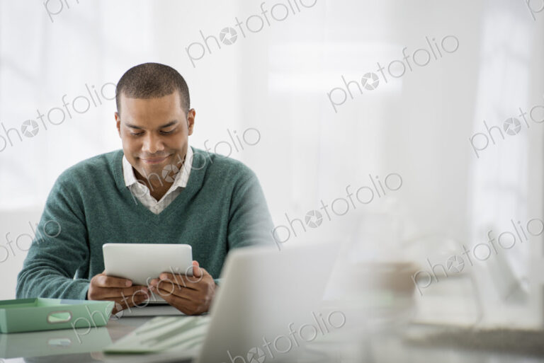 Business. A light airy office environment. A man sitting holding a digital tablet.