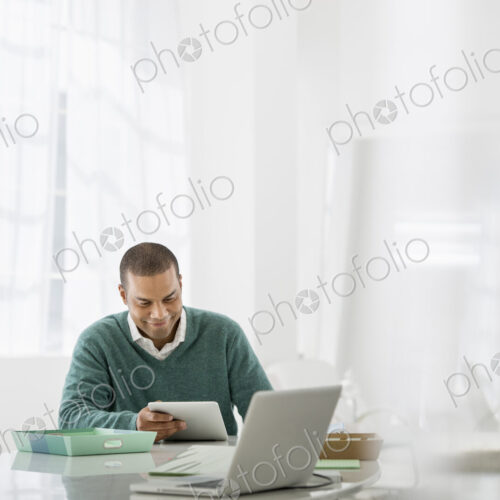 Business. A light airy office environment. A man sitting holding a digital tablet.