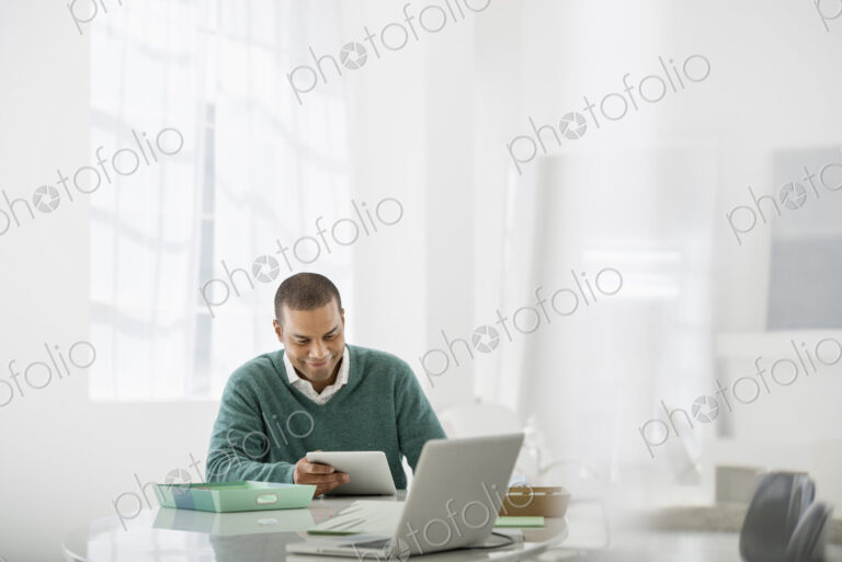 Business. A light airy office environment. A man sitting holding a digital tablet.