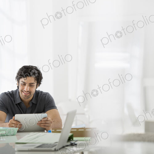 Business. A light airy office environment. A man sitting holding a digital tablet.