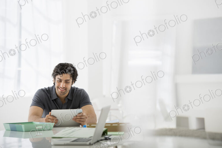 Business. A light airy office environment. A man sitting holding a digital tablet.