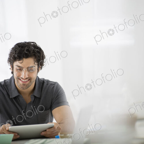 Business. A light airy office environment. A man sitting holding a digital tablet.