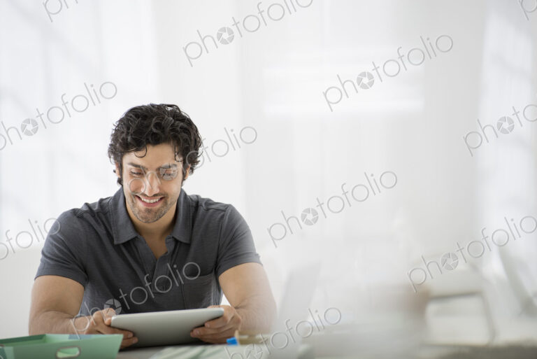 Business. A light airy office environment. A man sitting holding a digital tablet.