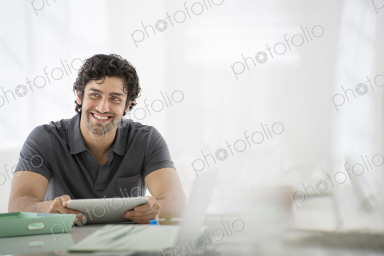 Business. A light airy office environment. A man sitting holding a digital tablet.