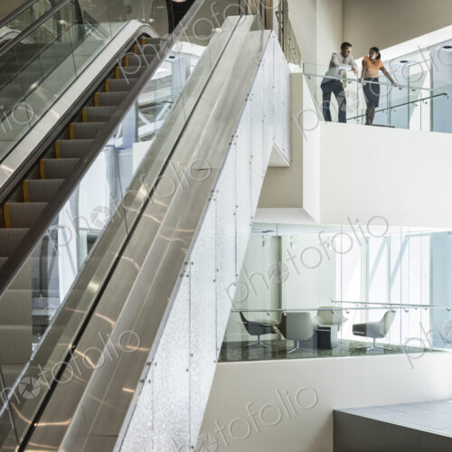 Businessman and woman at the top of an escalator in a large business center. Businessman and woman at the top of an escalator in a large business center.
