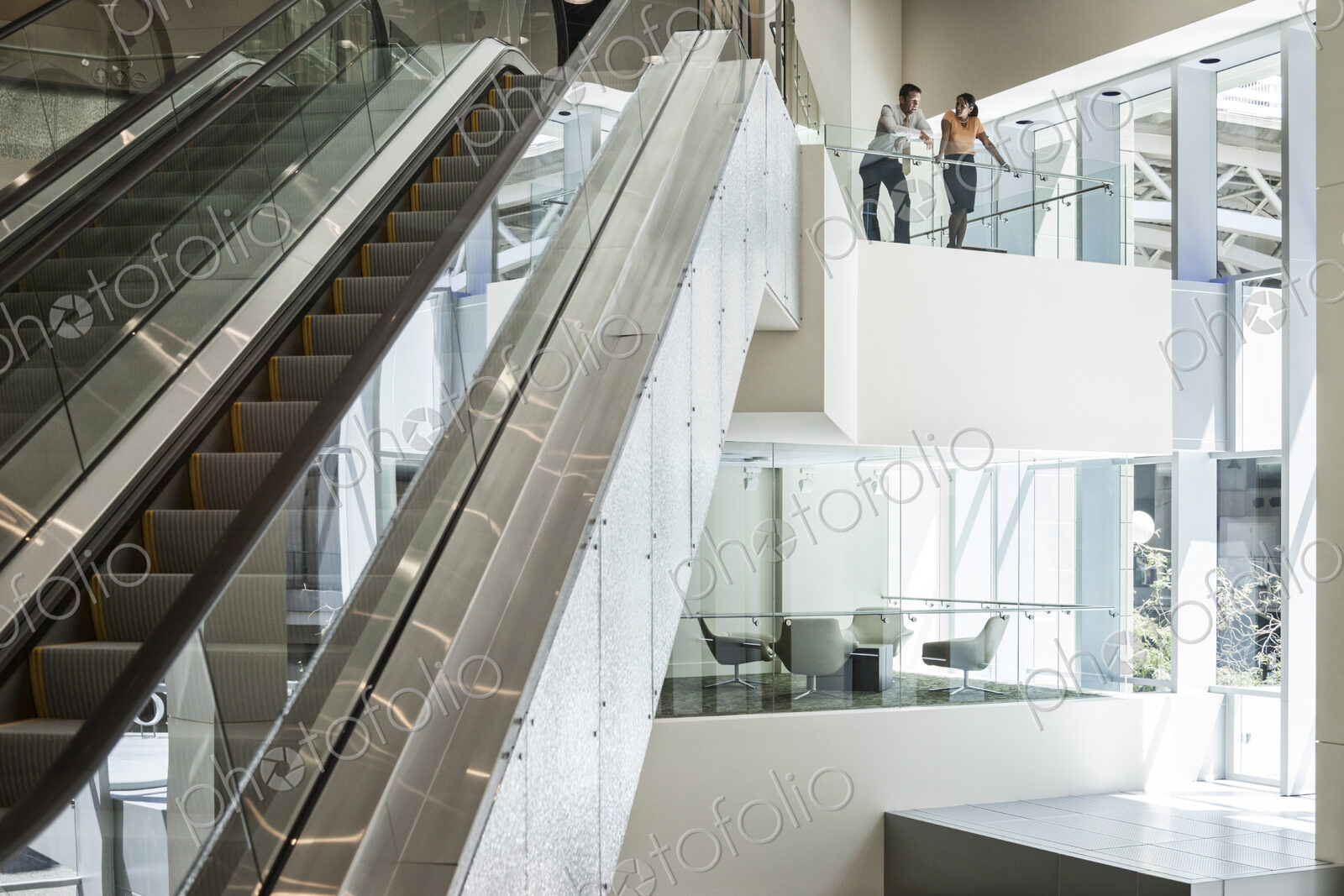 Businessman and woman at the top of an escalator in a large business center.