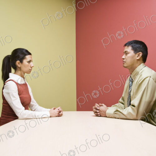Businessman and woman sitting on opposite sides of a conference table in a very…