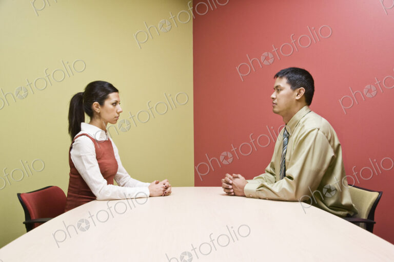 Businessman and woman sitting on opposite sides of a conference table in a very…