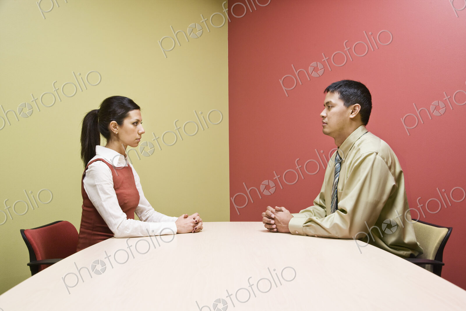 Businessman and woman sitting on opposite sides of a conference table in a very…