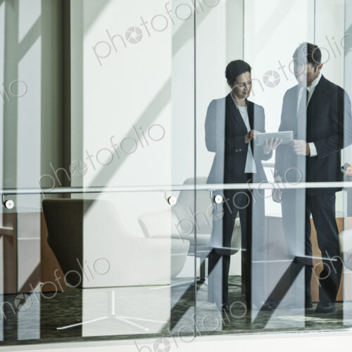Businessman and woman standing behind a conference room window in a large business center. Businessman and woman standing behind a conference room window in a large business center.