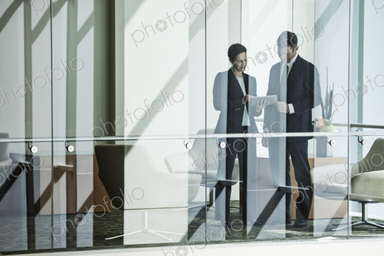 Businessman and woman standing behind a conference room window in a large business center.