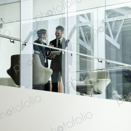 Businessman and woman standing behind a conference room window ina large business center.