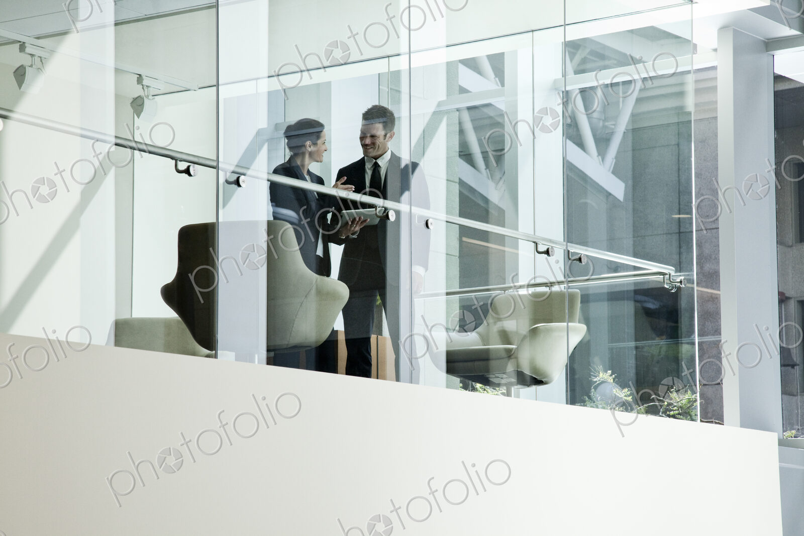 Businessman and woman standing behind a conference room window ina large business center.