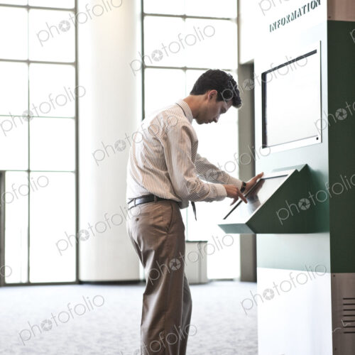 Businessman at an information kiosk in a large lobby area. Businessman at an information kiosk in a large lobby area.
