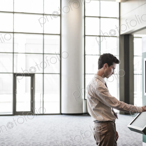 Businessman at an information kiosk in a large lobby area. Businessman at an information kiosk in a large lobby area.