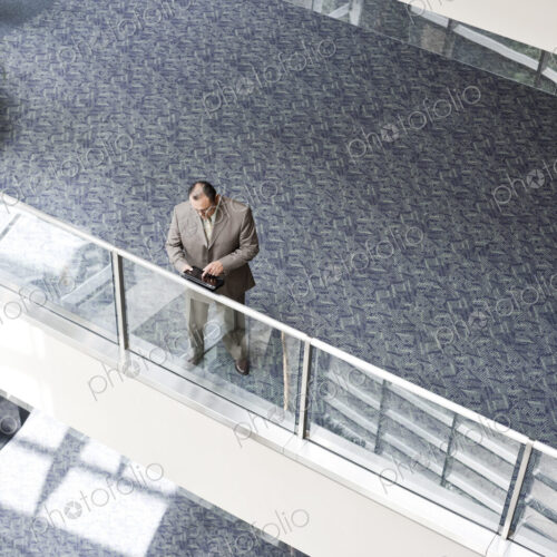 Businessman checking his notebook computer on a walkway, high angle view Businessman checking his notebook computer on a walkway, high angle view