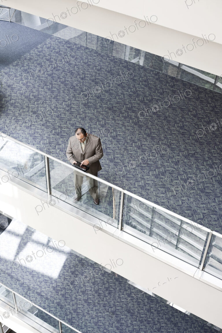 Businessman checking his notebook computer on a walkway, high angle view