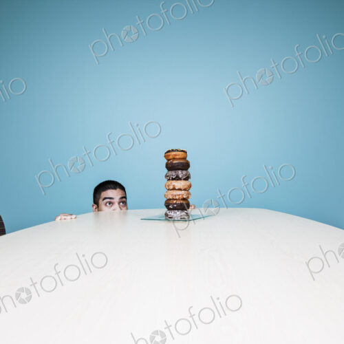 Businessman hiding behind a table with a stock of doughnuts on it. Businessman hiding behind a table with a stock of doughnuts on it.