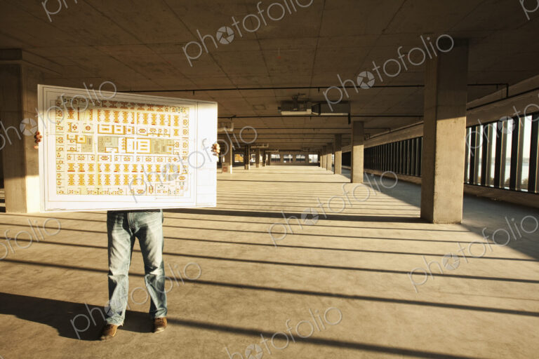 Businessman holding up plans for new office space standing in the middle of the empty…