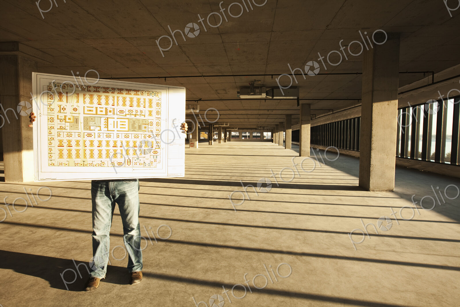 Businessman holding up plans for new office space standing in the middle of the empty…
