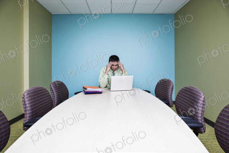 Businessman in a stressful situation sitting at a table in a conference room.