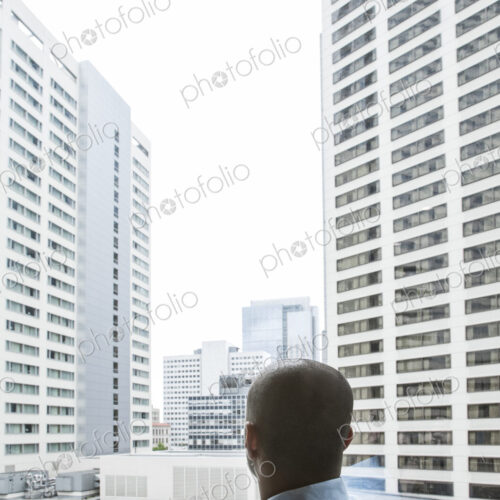Businessman looking out a window at a cityscape of tall buildings