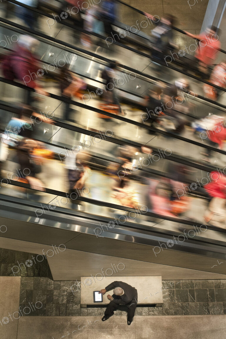 Businessman on a notebook computer near an escalator full of people.