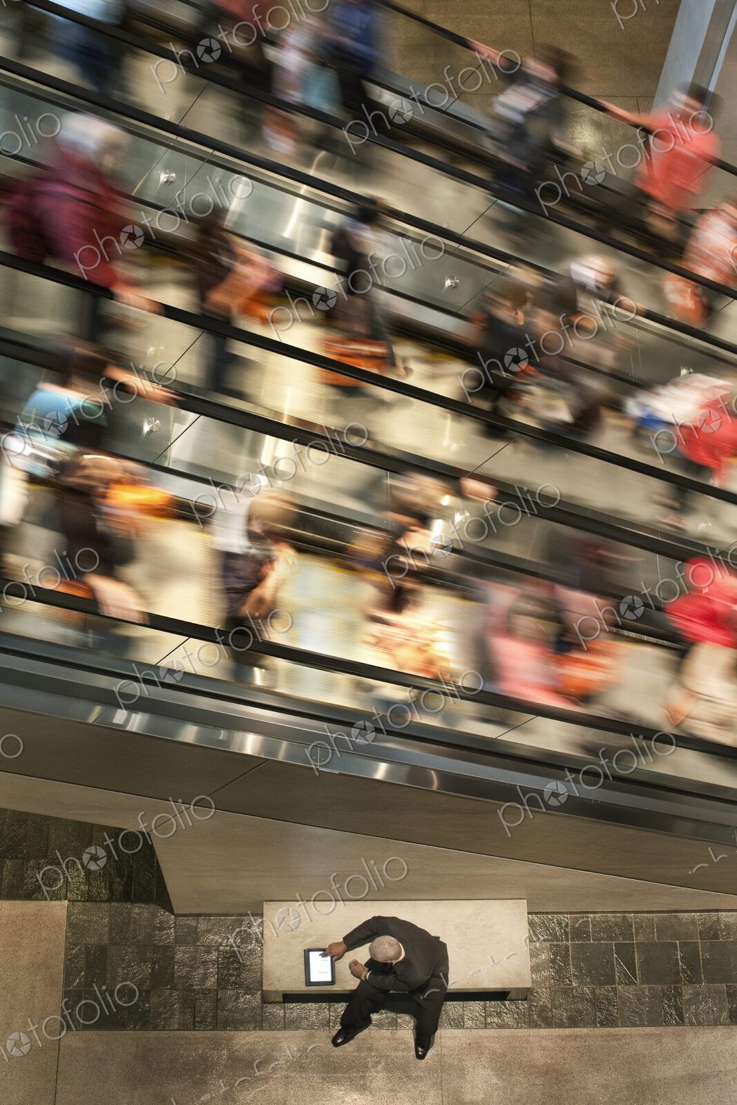 Businessman on a notebook computer near an escalator full of people.