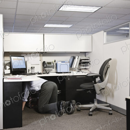 Businessman on his knees in his office cublice trying to connect a plug from a computer. Businessman on his knees in his office cublice trying to connect a plug from a computer.