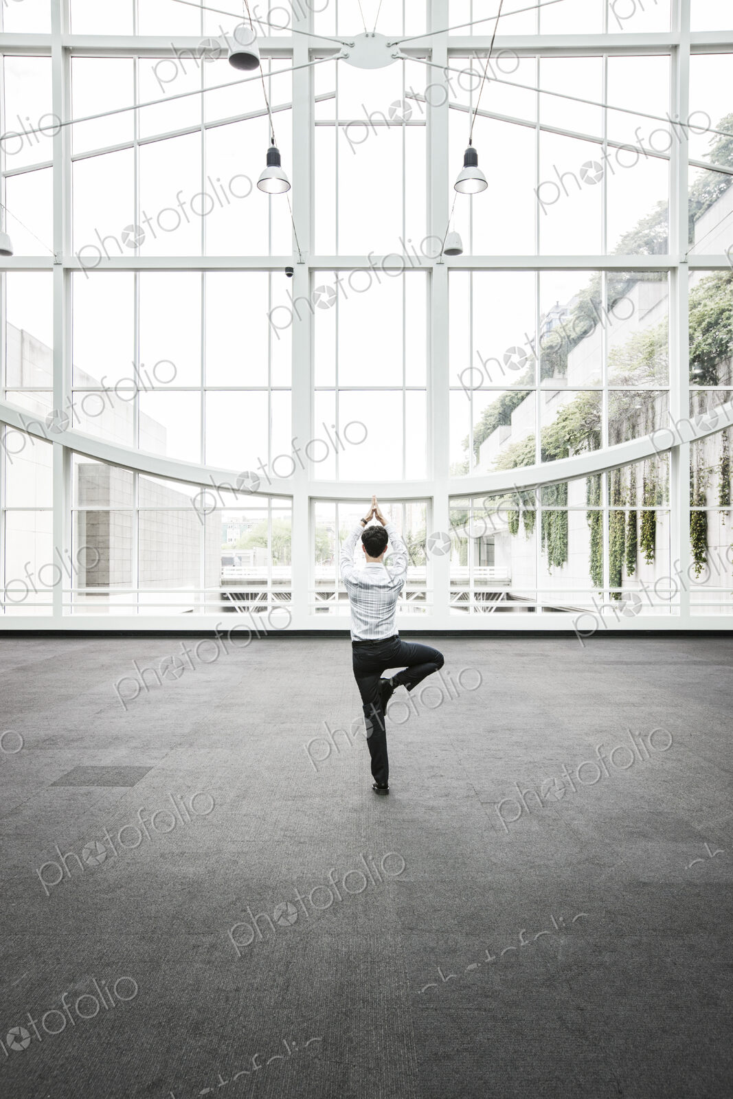 Businessman relaxing doing a yoga pose in a large open glass covered walkway.
