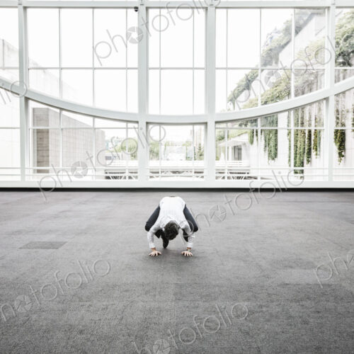 Businessman relaxing doing a yoga pose in a large open glass covered walkway.