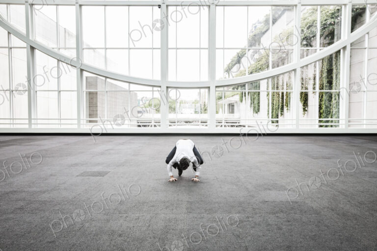 Businessman relaxing doing a yoga pose in a large open glass covered walkway.