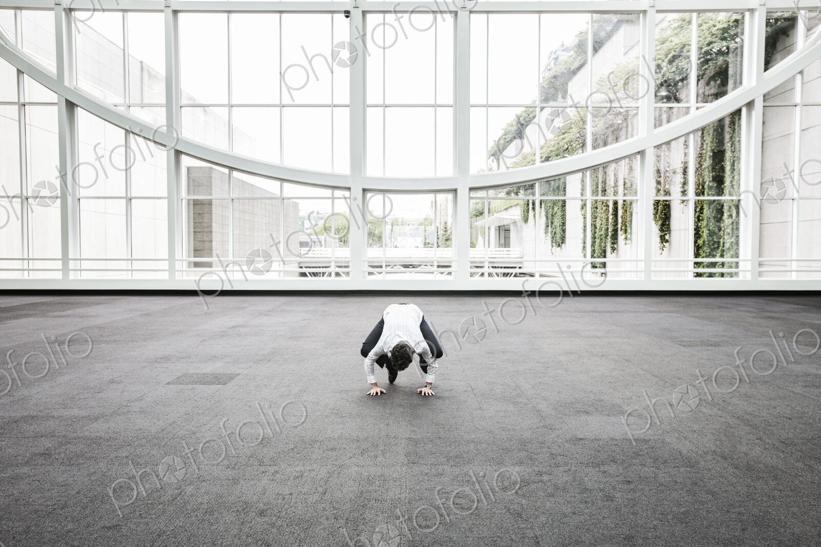 Businessman relaxing doing a yoga pose in a large open glass covered walkway.