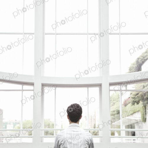 Businessman relaxing doing a yoga pose in a large open glass covered walkway.