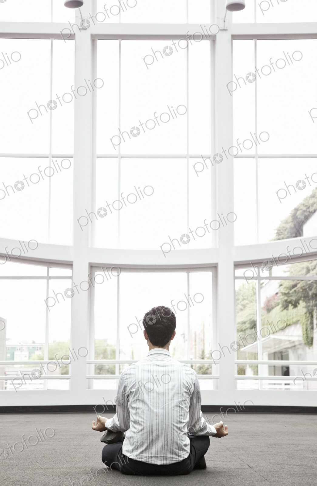 Businessman relaxing doing a yoga pose in a large open glass covered walkway.