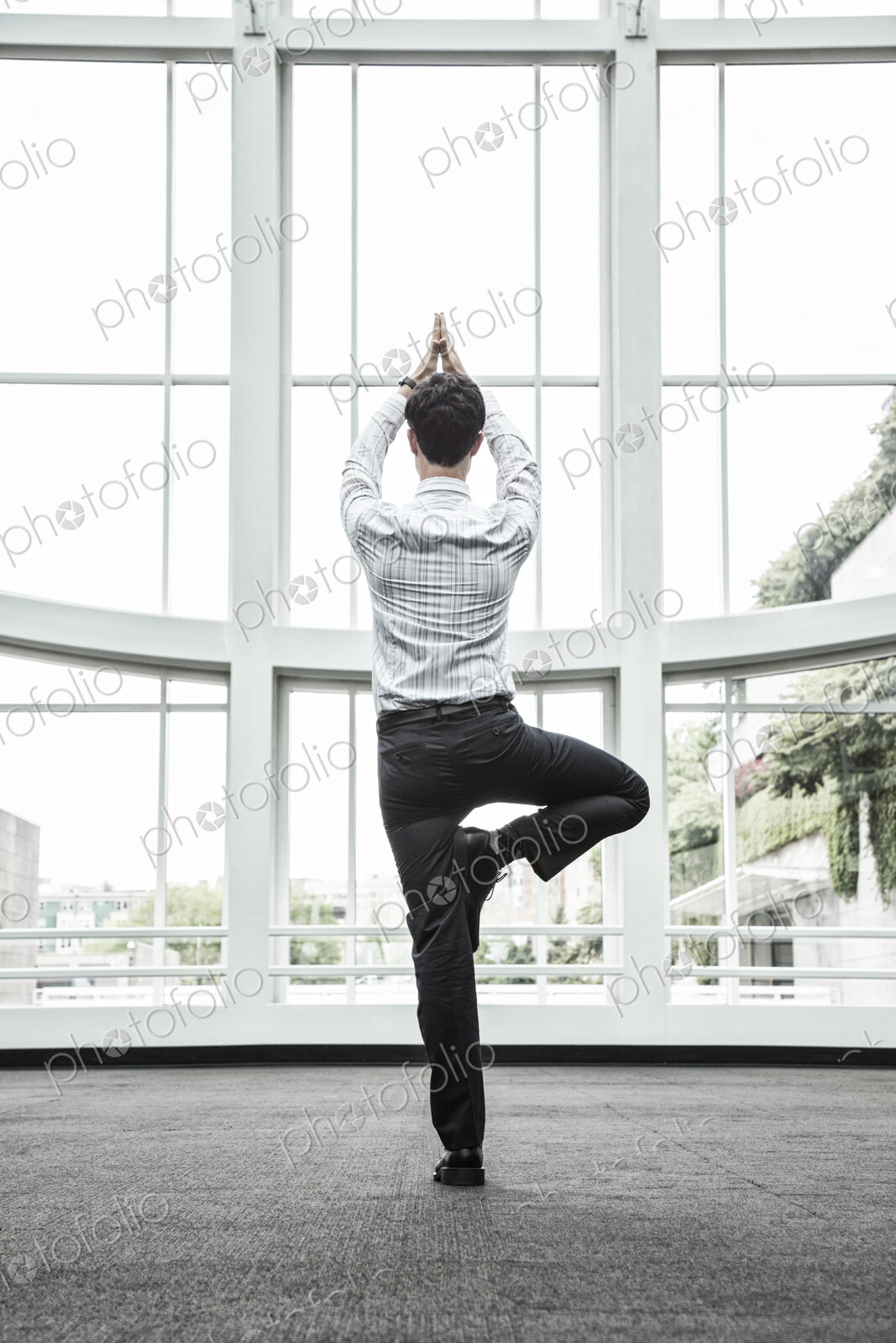 Businessman relaxing doing a yoga pose in a large open glass covered walkway.