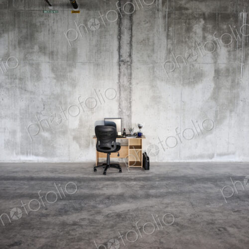 Businessman sitting at a small desk in a large empty raw office space.