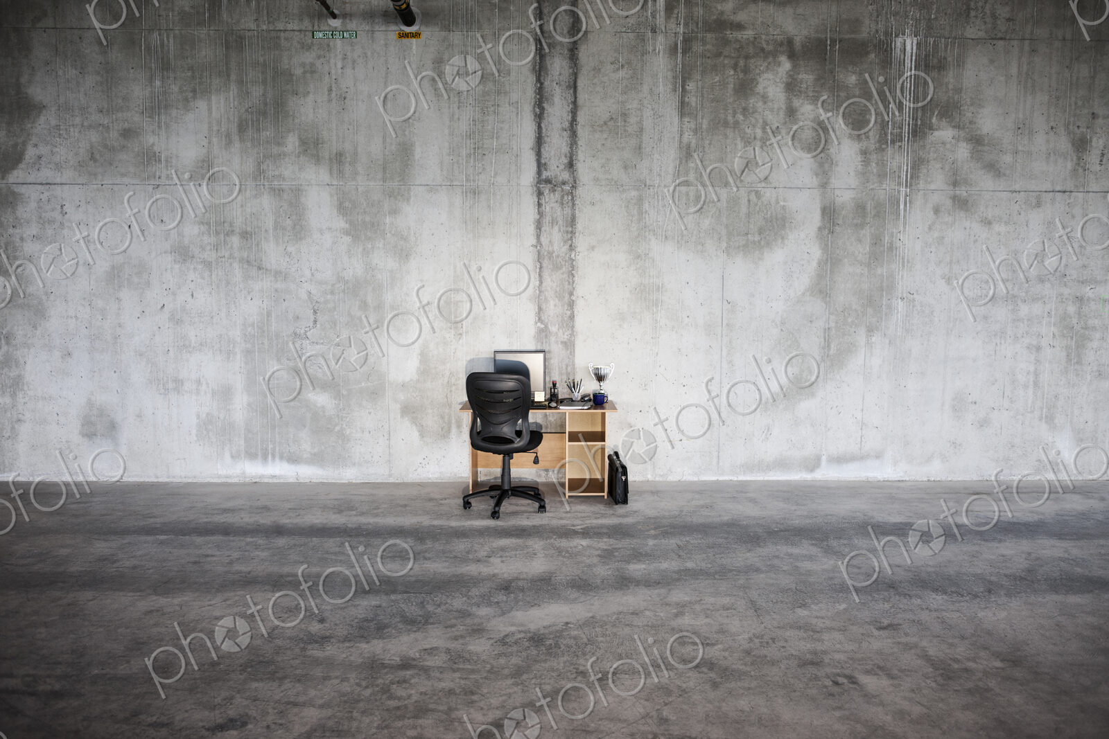 Businessman sitting at a small desk in a large empty raw office space.