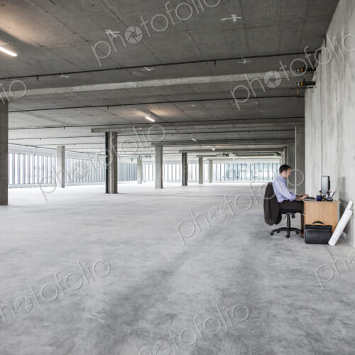 Businessman sitting at a small desk in a large empty raw office space.