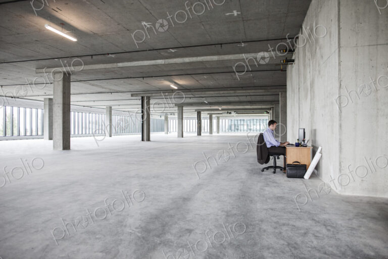 Businessman sitting at a small desk in a large empty raw office space.